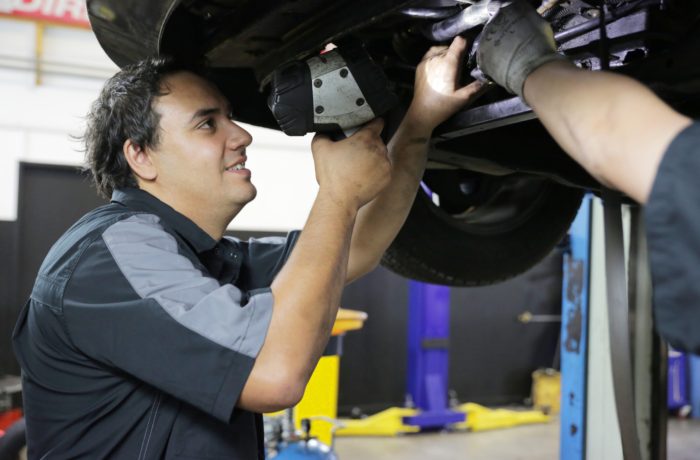 An Autoland mechanic underneath a car, conducting a WOF inspection.