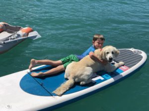 Little kid Mason beside a white dog in a surf baord floating on blue waters