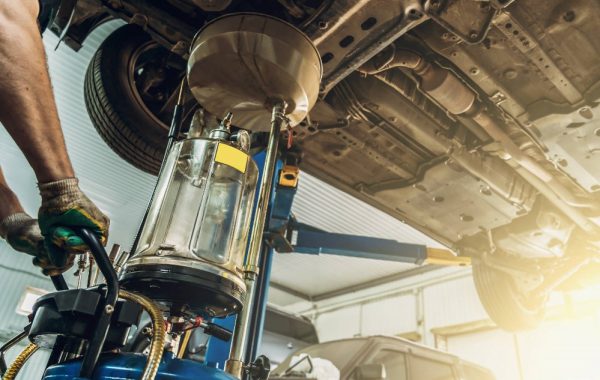 Mechanic drains oil from car on a lift