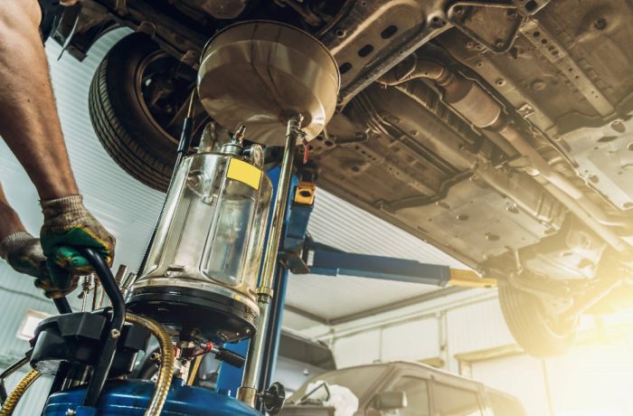 Mechanic drains oil from car on a lift