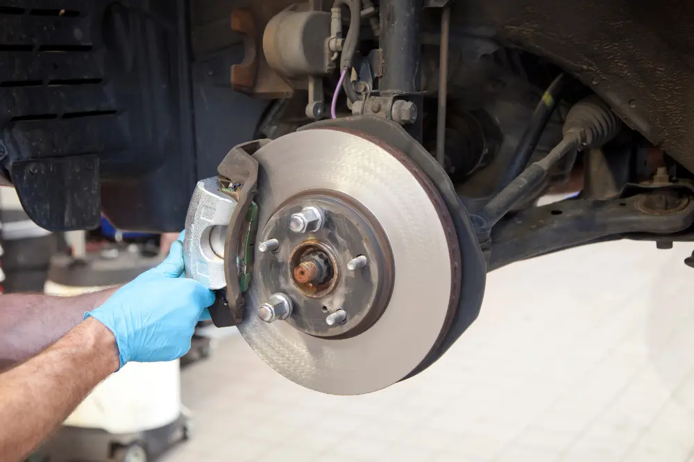 Mechanic wearing blue gloves servicing a car’s brake caliper beside an exposed brake disc