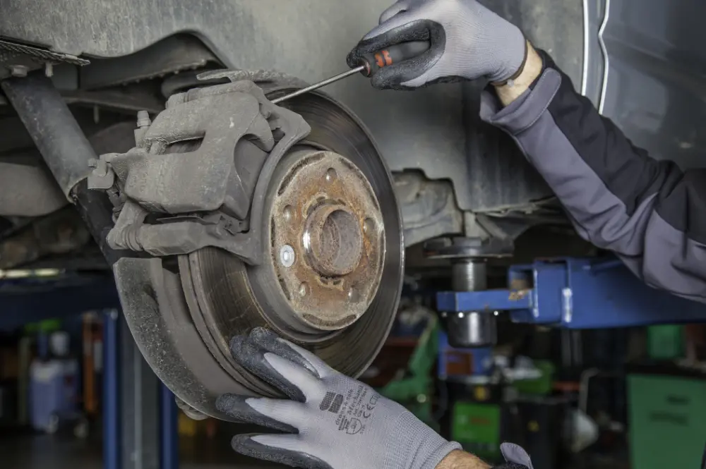 Mechanic inspecting a car’s brake disc and caliper with the wheel removed