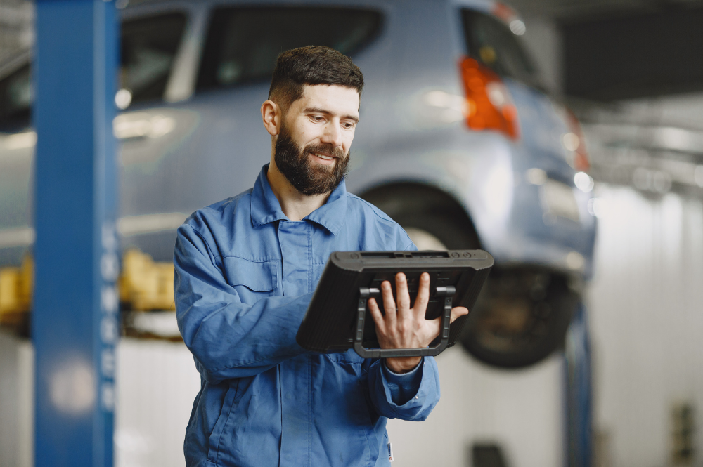 Mechanic using a diagnostic tablet beside a car raised on a workshop lift