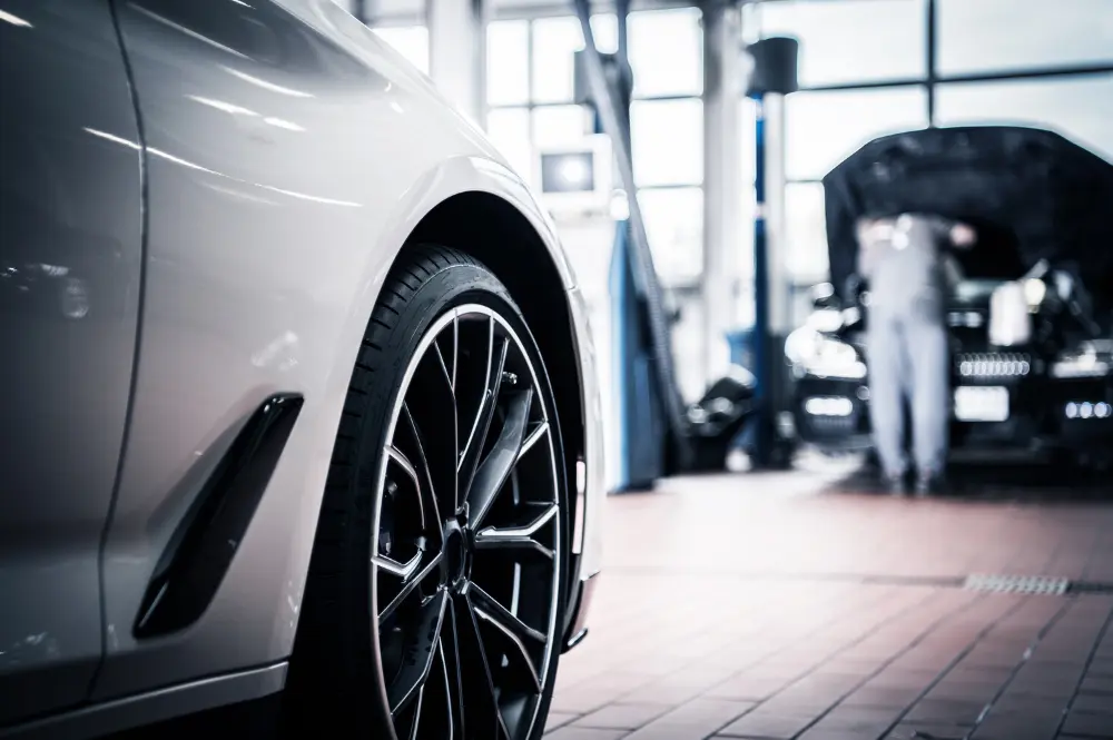 Cars in a servicing workshop with a mechanic working under an open bonnet
